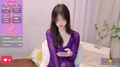 Media: Video of a young East Asian woman with long black hair, wearing a sheer purple robe, seated on a white chair in a modern, minimalist room.