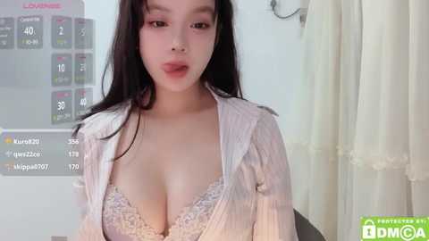 Media: Video of an East Asian woman with fair skin and long black hair, wearing a white blouse and lacy bra, in a dimly lit room with a digital thermometer.