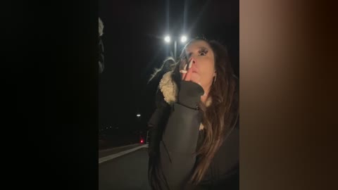 Media: A video depicts a woman in a dark coat and gloves, smoking a cigarette on a dimly lit highway at night.