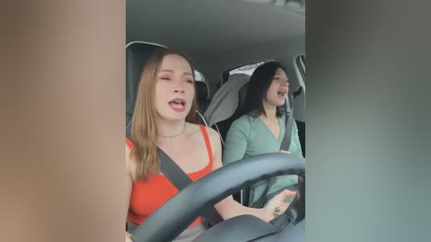 Media: Video of two young women, one with long blonde hair in an orange top, another with long black hair in a green top, laughing in a car.