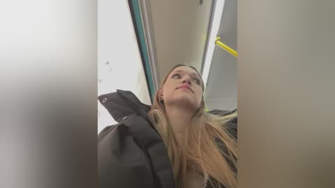 Media: A video of a young blonde woman with straight hair, wearing a black jacket, looking up in an airplane aisle.