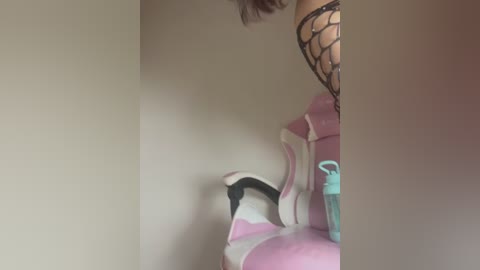 Media: Video of a person's legs in a black fishnet stocking, wearing pink high heels with a white base, standing in a dimly lit room.