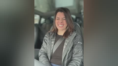 Media: A video of a smiling woman in a puffy gray jacket and brown shirt, riding in a car, with blurry car interior and windows in the background.