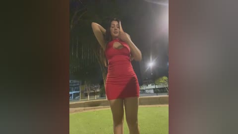 Media: Video of a young woman with long dark hair, wearing a tight red dress, standing confidently in a stadium under bright stadium lights.