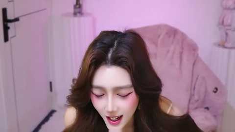 Media: Video of a smiling East Asian woman with long brown hair, wearing pink lipstick, in a white room with a pink towel.