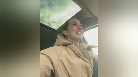 Media: A video of a smiling, light-skinned woman with brown hair in a beige jacket, seen from a car's backseat, gazing at greenery outside.