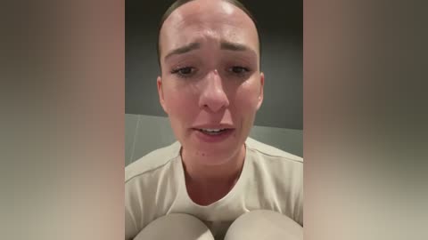 Media: Video of a bald Caucasian man with a pale complexion, wearing a white shirt, looking distraught, with blurred background.