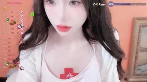 Media: Video of a young Asian woman with pale skin, long dark hair, and light makeup, wearing a white tank top with a red cross, standing in a peach-colored room.