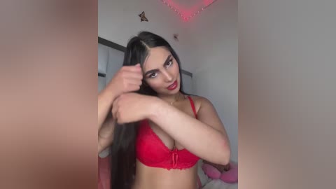 Media: Video of a young woman with long black hair, fair skin, and full lips, wearing a red lace bra, adjusting her hair in a bedroom with pink lights and a star decoration on the wall.