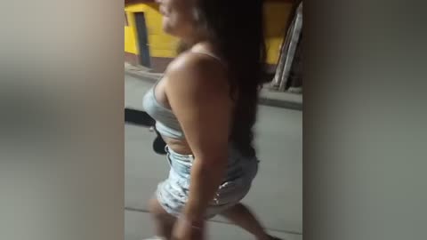 Media: A blurry video of a woman with long, dark hair in a tight, sleeveless white dress walking away, her backside prominent. Background features yellow and black objects.