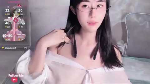 Media: A video of an Asian woman with long black hair and glasses, wearing a white off-shoulder blouse, in a dimly lit room. Background includes a monitor showing a virtual character, and a \"Follow Me\" button.