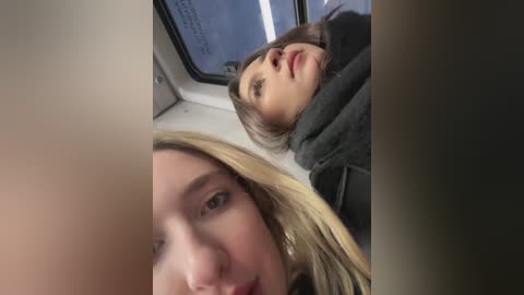 Media: Video of two women in a train, one with blonde hair, another with brunette hair, looking up, blurred background.