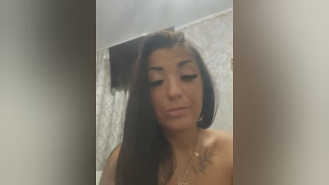 Media: Video of a Latina woman with long, dark hair and medium skin tone, wearing minimal makeup, in a bathroom with a tiled wall.