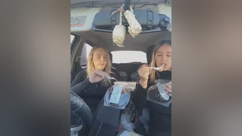 Media: Video of two women with long hair eating ice cream cones while sitting in a car with a view of a parking lot outside.