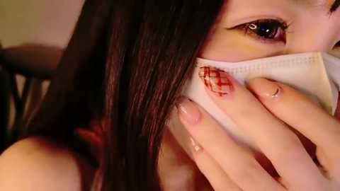 Media: Video of a young woman with long, straight black hair and fair skin, wearing a white mask with a red stain, suggesting she's coughing.