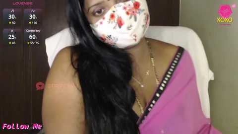 Media: A video shows a South Asian woman with long black hair, wearing a floral mask, pink saree, and white shirt. Background includes a wooden door and a pink Follow Me watermark.