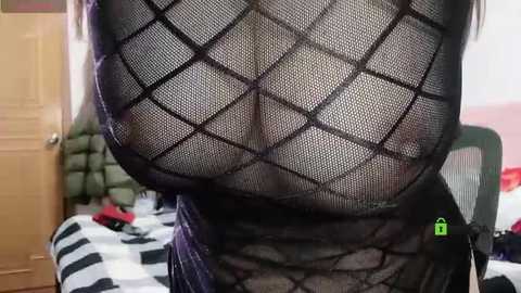 Media: Video of a woman's torso in a black, see-through mesh top, showing her ample breasts and nipples. Background shows a door, bed, and red blanket.