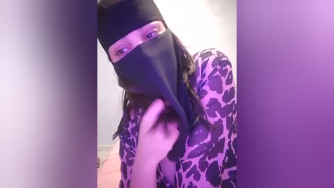 Media: A video of a person with light skin, wearing a black mask and leopard print shirt, standing in a dimly lit room.