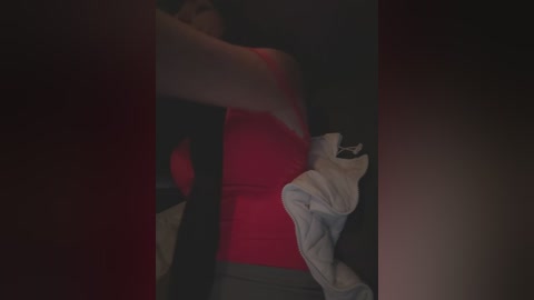 Media: A dimly lit video captures a woman in a red tank top and gray pants, holding a white shirt, with a blurred background.