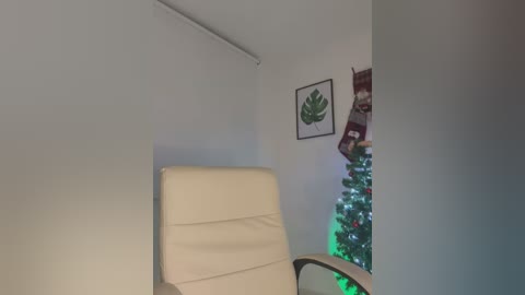 Media: A video of a cozy room with a beige leather chair, white wall, framed leaf art, and a festive Christmas tree with multicolored lights.