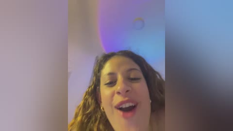 Media: A video captures a smiling, curly-haired woman with light brown skin, eyes closed, and mouth open, set against a blurred, multi-colored background.