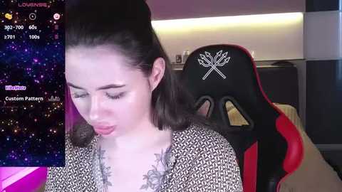 Media: Video of a young Asian woman with fair skin, dark hair in a high ponytail, wearing a black and white patterned dress, sitting in a red and black gaming chair in a dimly lit room with a starry night background on a computer screen.