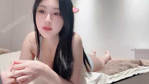 Media: A video of a young Asian woman with long black hair and fair skin lying on a bed, wearing light blue panties, in a minimalistic, modern bedroom setting.