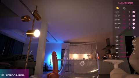 A video of a dimly lit, modern living room with a large, realistic, orange dildo on the floor, a gold lamp, and a glass table, with streaming video text overlay.