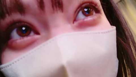 Media: Close-up video of a person wearing a white surgical mask covering the nose and mouth, with their eyes and eyebrows visible, emphasizing concern and vigilance during a pandemic.