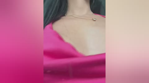 Media: Video of a woman with light skin, wearing a bright pink, low-cut top, showcasing her cleavage and a gold necklace. The background is blurred, emphasizing the woman's attire and jewelry.