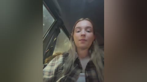 Media: A video shows a young woman with light skin and long blonde hair, wearing a plaid shirt and looking out the window of a car.