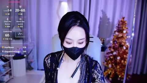 Media: Video of an Asian woman with pale skin, black hair, wearing a black mask and lace cardigan, indoors with a Christmas tree and purple curtains.