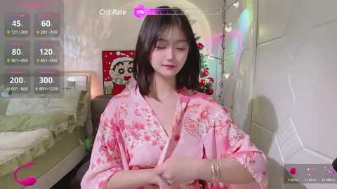 Media: Video of a young Asian woman with shoulder-length black hair, wearing a pink floral kimono, sitting on a bed with a Christmas-themed pillow in a softly lit room.