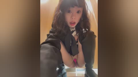 Media: Video of an Asian woman with long, wavy brown hair, wearing a black jacket, lifting her breasts, revealing pink bra. She has a surprised expression. Background is blurry.