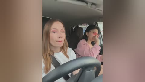 Media: Video of two women in a car: a blonde in a white shirt driving, and an Asian woman with glasses and pink top in the passenger seat.