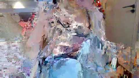 Media: Video of a chaotic, abstract scene with blurred, multi-colored objects, possibly toys or household items, scattered on a white surface, creating a surreal, disorganized mess.