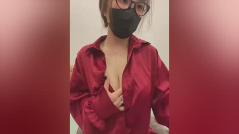 Media: Video of a woman in a red satin blouse with a black mask, glasses, and a cleavage reveal, against a blurred red background.