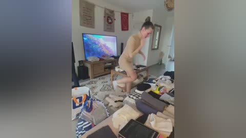 Media: A candid video shows a young woman in beige lingerie dancing energetically on a messy living room floor. The room is cluttered with clothes and electronics, including a TV and various posters on the wall.