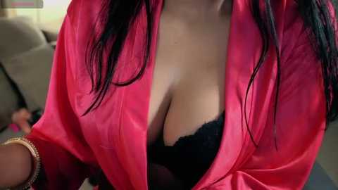 Media: Video of a woman with medium brown skin and long, straight black hair, wearing a red satin robe that exposes a black lace bra, revealing cleavage.