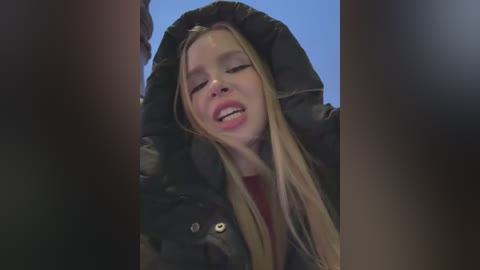 Media: Video of a blonde, Caucasian woman with a puffy black jacket, looking upward with her mouth open, surrounded by blurred, dark figures.