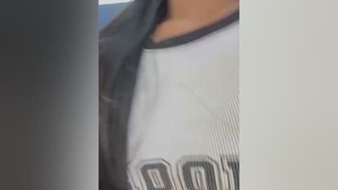 Media: A close-up video of a person wearing a white, ribbed sports jersey with black \"BOSTON\" text, and a black jacket, blurred background.