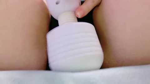 Media: A close-up video of a white hand using a white, ribbed wand vibrator on a person's vulva, with the person's thighs and labia visible, suggesting a focus on sexual stimulation.