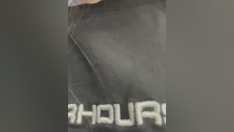 Media: A close-up video of a person wearing a black t-shirt with white \"3 HOUR\" text, the fabric appears slightly wrinkled. The background is blurred and dark.