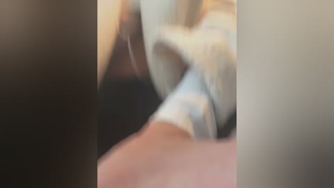 Media: A blurry video of a close-up of a person's hand and arm, possibly in a white shirt, in a dimly lit room. The image lacks clarity and details.