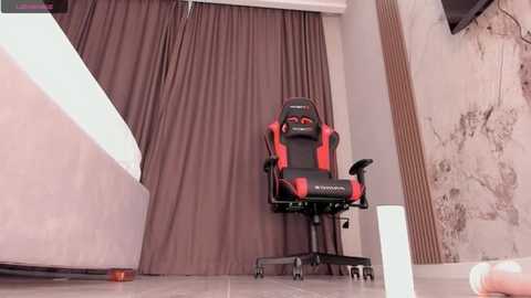 Media: Video of a modern gaming setup with a red and black Razer chair, beige curtains, and a partially visible white wall with brown wooden paneling.