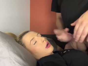 Media: A video of a blonde woman with fair skin lying on a bed, wearing black lingerie, eyes closed, mouth slightly open, receiving oral sex from a man in black clothing.