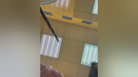 Media: Video of a modern, bright classroom with yellow walls, blue rectangular tiles, white blinds, and a ceiling fan, featuring a blurry figure in the foreground.