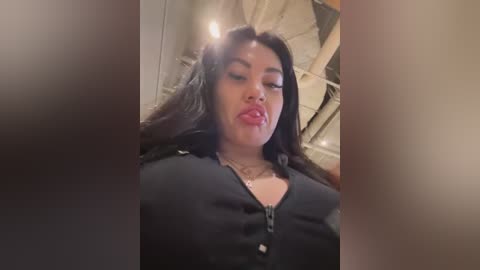 Media: Video of a curvy Black woman with long black hair, wearing a black zip-up top, puckering her lips in a sultry pose against a blurred, rustic wooden background.