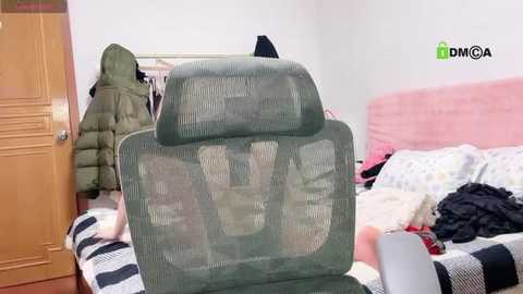 Media: A video of a messy bedroom with a green mesh chair, clothes, and a pink bedspread; a wooden door is visible on the left.