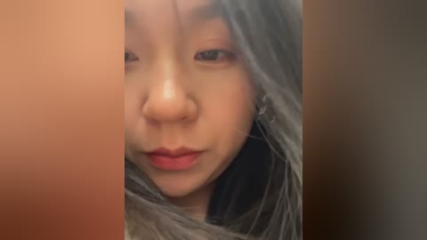 Media: A video of an Asian woman with light skin, wearing a grey, see-through scarf that covers her head and partially her face, revealing her brown eyes and pink lips.